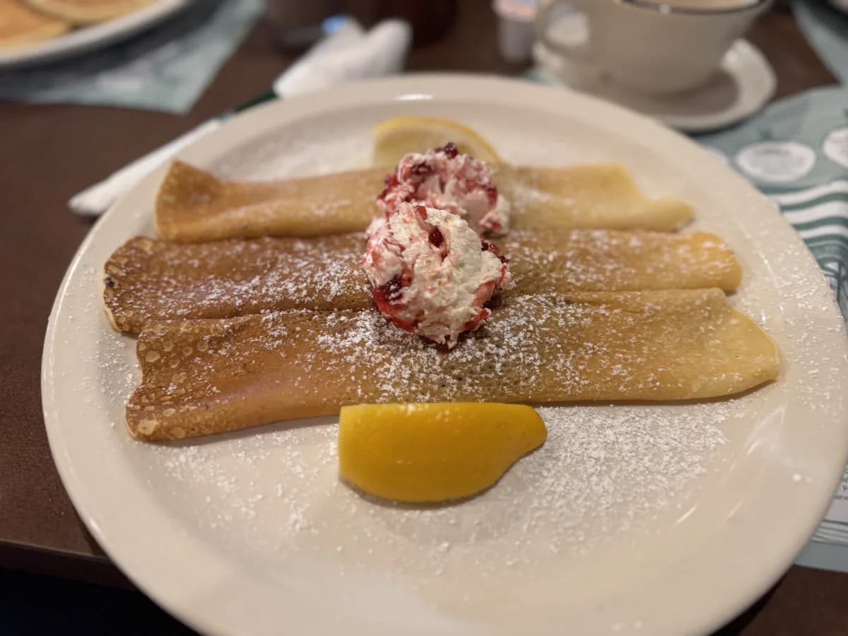 Three crepes topped with whipped cream and strawberries, dusted with powdered sugar, served with lemon wedges. at Pancake Pantry in Gatlinburg